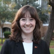 Emily, a white woman with golden brown hair, wears a white shirt and black blazer.