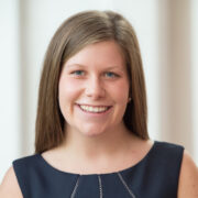 Sadie, a white woman with light brown hair, wears a navy blue sleeveless dress. 