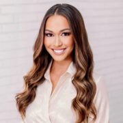 Alexandria, a white woman with long brown hair, wears a white blouse. 